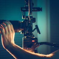 Caucasian Videographer. Professional Camera Operator with Pro Digital Equipment Taking Indoor Video Shots For Documentary Short Film.